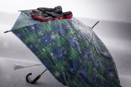 Red winter gloves leaning on an umbrella under the snows. Concept of cold, bad weather and winter, Selective focus on the gloves and copy spaceの写真素材
