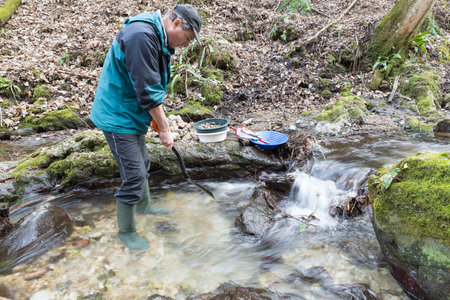 Outdoor adventures on river. Gold panning, search for gold. Man is looking for gold with a shovel in hand in a small streamの写真素材