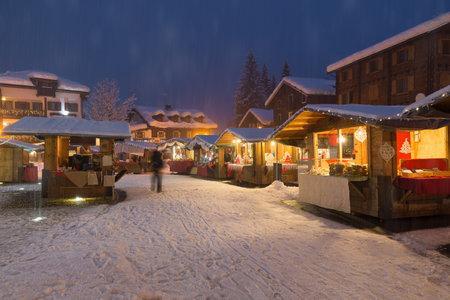 Illuminated stalls in the evening during the Christmas period at a mountain village in the European Alps during a heavy snowfall, Macugnaga, north Italyの写真素材