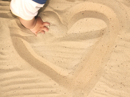 Child playing with sand, drawing a heart in the sandの写真素材