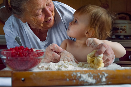 Portrait of faces, hands happy gray-haired granny, granddaughter. toddler girl play with baking, dough, flour on kitchen. child baby try cooking cookies, cake. Cozy family Look at each otherの写真素材