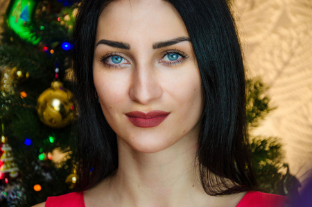 portrait of attractive caucasian smiling woman black hair on studio shot. caucasian girl with blue eyes near christmas tree.の写真素材