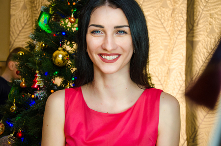 portrait of attractive caucasian smiling woman black hair on studio shot. caucasian girl with blue eyes near christmas tree.の写真素材