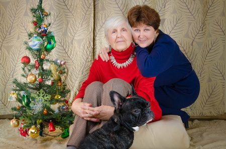 Family moments at Christmas time. old woman smile. grandmother and her daughter are sitting near Christmas tree. spirit of New Year. hug each otherの写真素材