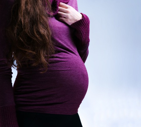 full length of caucasian, pregnant woman stay in studio. close up on the stomach. with out hand on belly. happy pregnancy. purple sweater. pregnant body. dark lightの写真素材