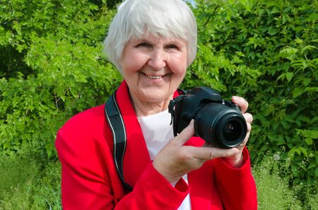 portrait of smile, happy grandmother enjoy her hobby at sun day. modern granny is professional photographer . photocamera in adult hand of old lady. pensioner use technologyの写真素材