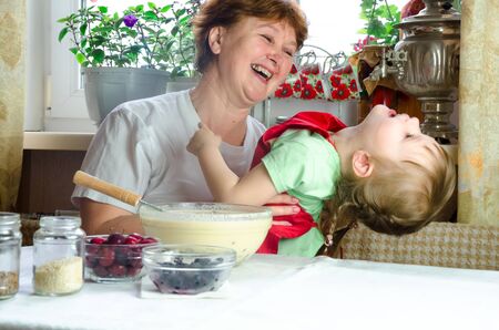 Portrait of faces, hands happy granny hug granddaughter. toddler girl play with grandmother on kitchen. child baby hold grandma and laugh . Cozy family Look at each otherの写真素材