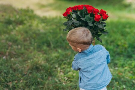 Boy with a bouquet of red roses in hands on a background of greenery.の写真素材