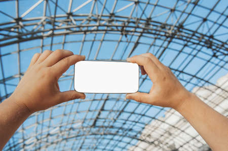 A man holds a smartphone in his hands on the background of an iron structure.の写真素材