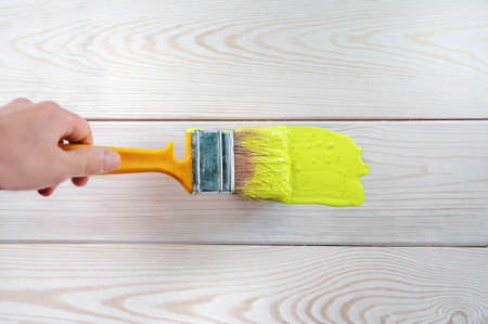Closeup female hand with paintbrush painting a natural wooden door with yellow paint. The concept of colored bright creative interior design for a young family. How to paint a wooden surface.の写真素材