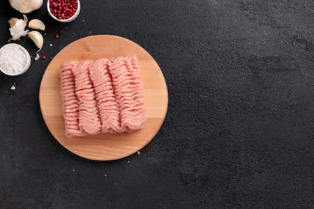 Raw mincemeat, poultry farce meat portion on a wooden board on a black background