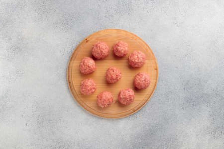 Top view of raw meat balls on a round wooden board