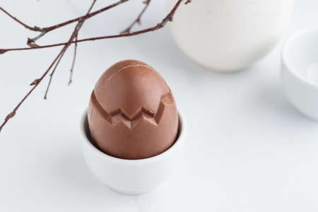 Chocolate easter egg in a white eggholder on a white tableの写真素材