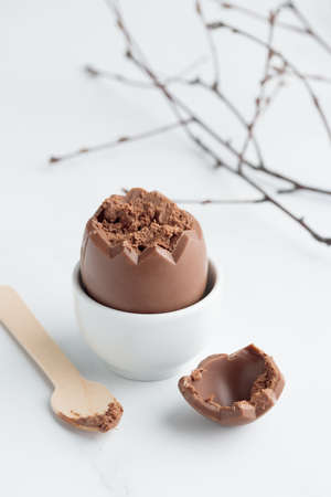 Chocolate easter egg in a white eggholder on a white tableの写真素材