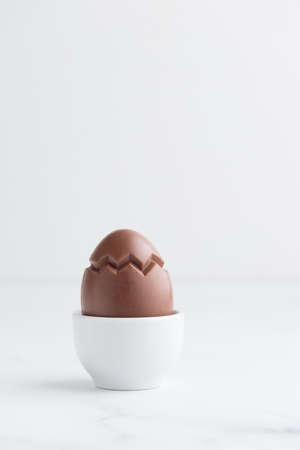 Chocolate easter egg in a white eggholder on a white tableの写真素材