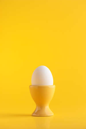 White egg in a stand on yellow background