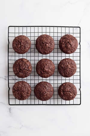 Freshly baked chocolate muffins on a grid on white table
