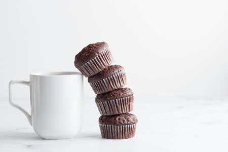 The stack of chocolate muffins with a white mug on a white tableの写真素材