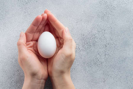 Human hands holding a white egg gray backgroundの写真素材
