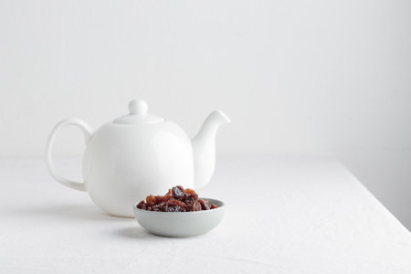 White teapot with raisins on a table on a white backgroundの写真素材