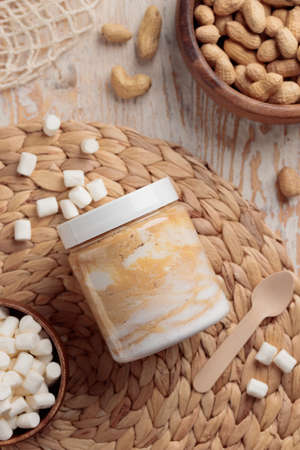 Jar with peanut butter and sweet ingredients on white wooden background closeup