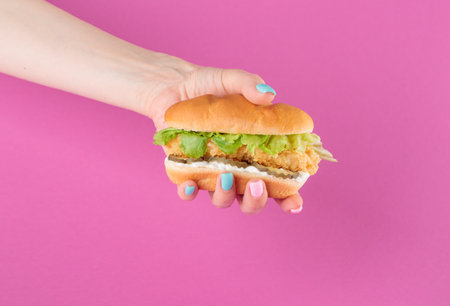 Female hand with tasty burger on a pink backgroundの写真素材