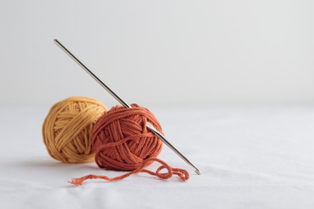 Crochet hook and a small balls of yellow and orange yarn on a white backgroundの写真素材