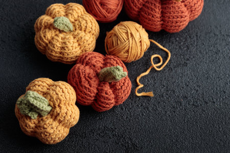 Cute crochet knitted yellow and orange pumpkins on black background with a ball of yarn and hook and a copy spaceの写真素材