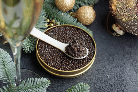 Black caviar in a mother-of-pearl spoon with Christmas decoration Horizontal on a black background with a copy spaceの写真素材