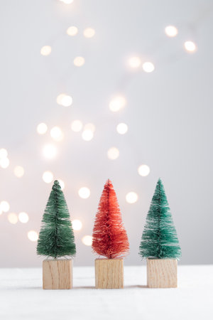 Three cute Christmas miniature fir trees on a white table with bokeh lights Vertical with copy spaceの写真素材