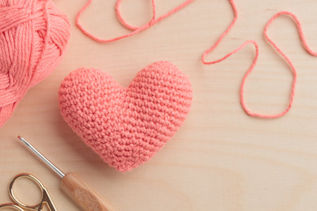 Crocheted amigurumi pink heart with crochet hook and a yarn on a wooden background. Valentine's day...