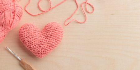 Crocheted amigurumi pink heart with crochet hook and a yarn on a wooden background. Valentine's day banner with a copyspaceの写真素材