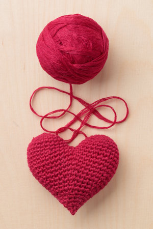 Crocheted amigurumi pink red heart on a wooden background with a skein of yarn. Valentine's day...