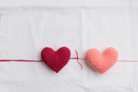 Two crocheted amigurumi pink hearts connected with a knot on a white background. Valentine's banner top view with copyspaceの写真素材