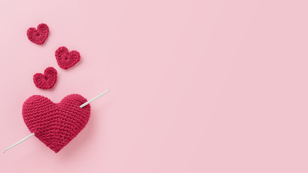 Crocheted amigurumi purple red burgundy heart with crochet hook on a pink background. Valentine's day banner with a copyspaceの写真素材