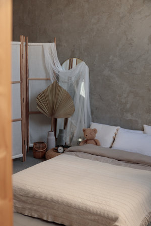 Cozy bedroom with pillows, knitted beige plaid, candles and alarm clock