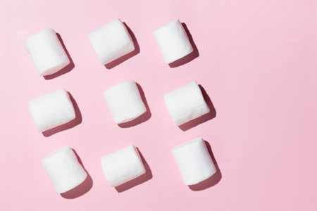 Rows of white marshmallows pattern on light pink table background in hard light. Pastel color.の写真素材