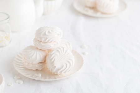 White airy zephyr or marshmallow shells on a plate on a white table- banner with space for text