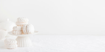 White airy zephyr or marshmallow shells on a cake stand on a white table- banner with space for textの写真素材