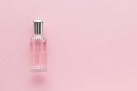 Transparent bottle of perfume on a pink background. Women's fragrance essence.