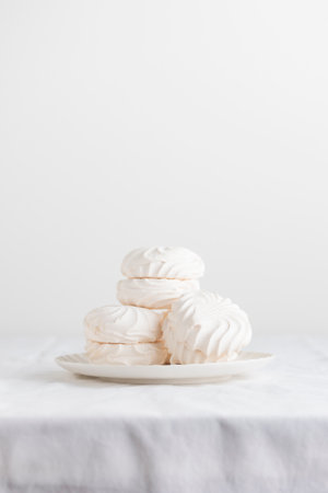 White airy zephyr or marshmallow shells on a plate on a white table- with space for textの写真素材