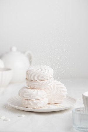 White fluffy marshmallows or marshmallow shells with powdered sugar sprinkles on a white plate on a white tableの写真素材