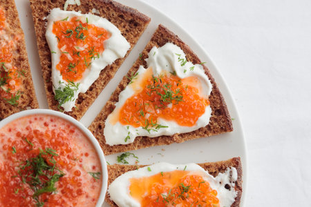 Homemade appetizer with red caviar, sour cream, dill, onion and rye bread on the white table - the...