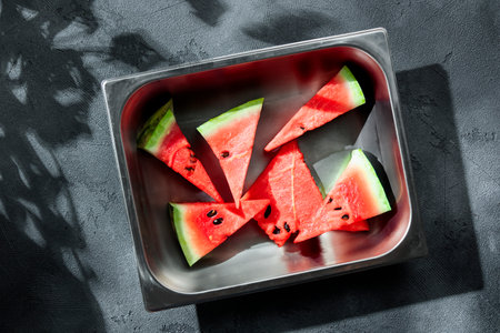Slices of juicy watermelon on the metal plate on the concrete background with summer sun shadows. Copy space. Top view.の写真素材