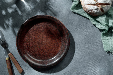 Brown rustic empty plate, cutlery and napkin on stone table top view, sunny day, shadows, summer....