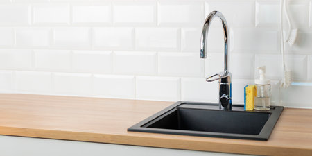 An empty black kitchen sink in a kitchen with a chrome faucet, wooden countertop, and white subway...