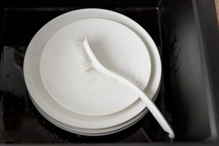 Washing of white plates dishes with brush in the black sink, tableware cleaning with soap foam conceptの写真素材