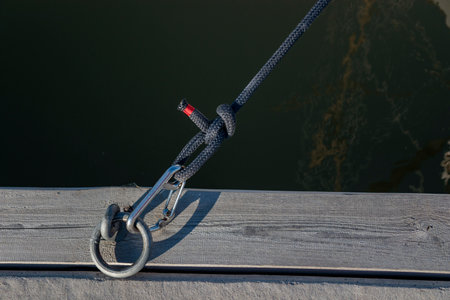 Mooring ring for boats in the port with carbine and black rope from the boat, wooden pier, sunny...