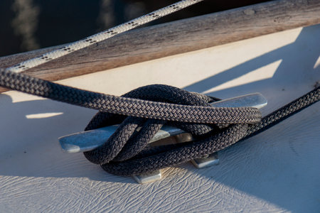 Black rope tied to the mooring cleat of a sailboat, sunny light, Finland