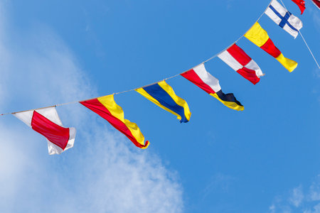 Diagonal hanging vibrant colorful nautical marine pattern signal system flags billowing on stretched cable lines with blue sky backgroundの写真素材